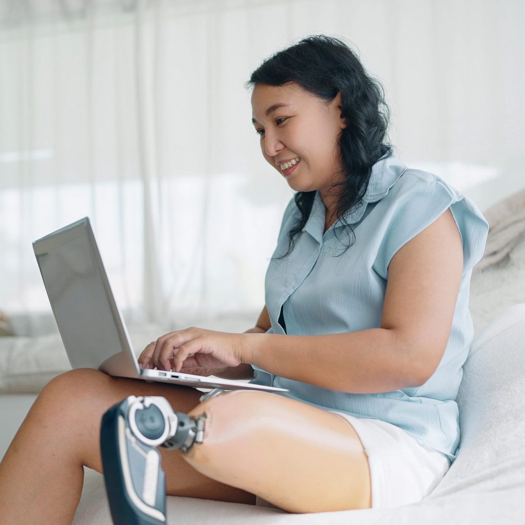 Happy adult woman with prosthetic leg typing on laptop.