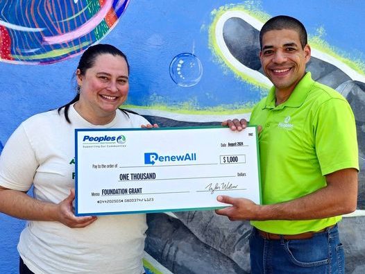 A Peoples Bank associate presents a $1,000 check to a RenewAll Inc employee.