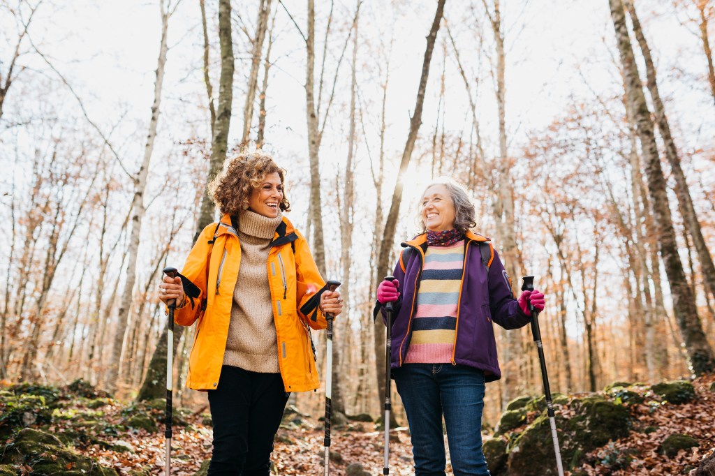 Two senior female friends hiking together through the forest in autumn.