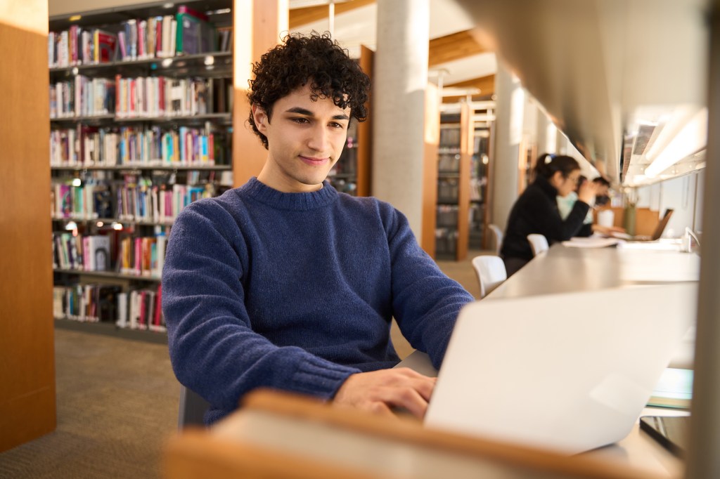 Male student using laptop, focused on working on a diploma project.