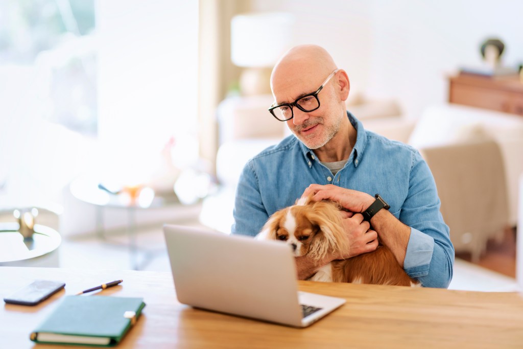 Middle aged man with his puppy sitting at home and working from home.