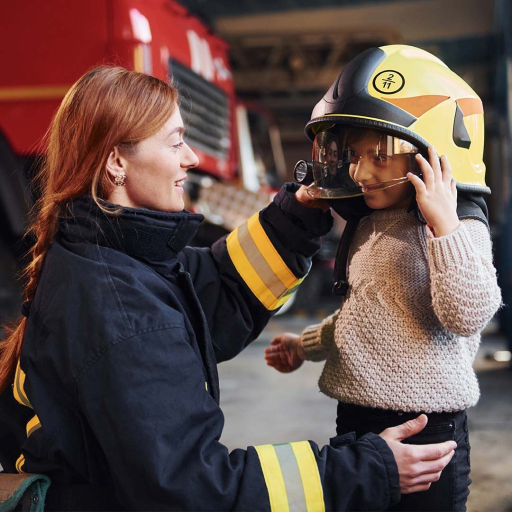 Happy little girl is with female firefighter in protective uniform.