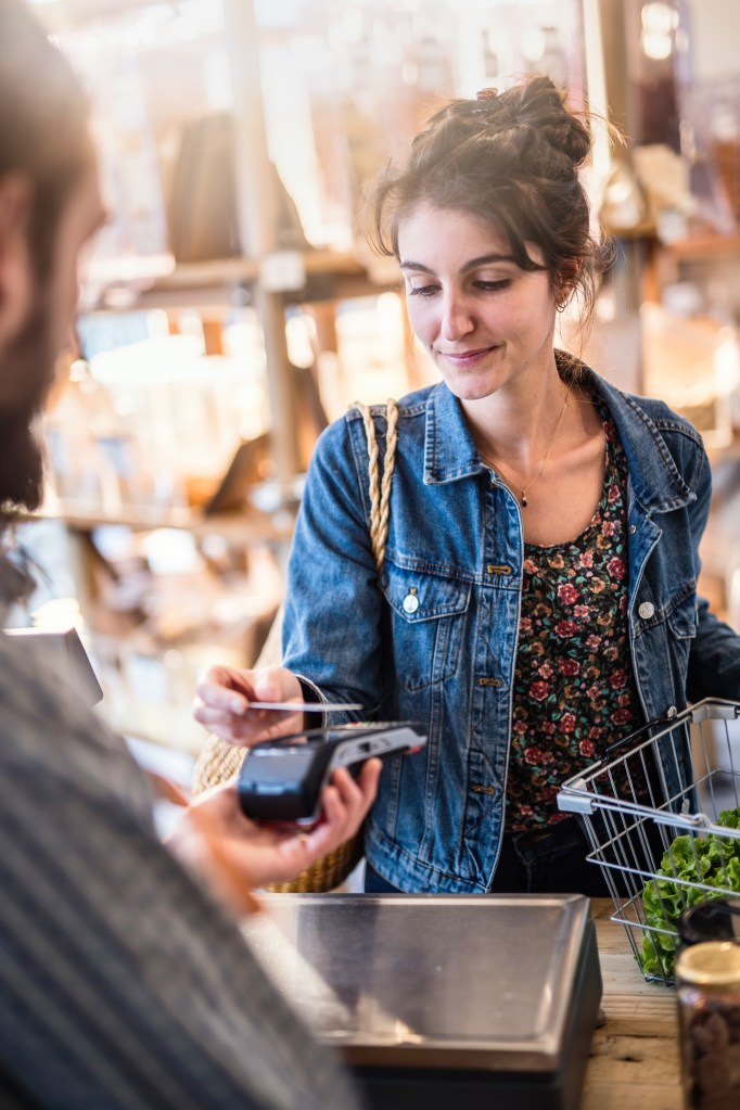 A young woman makes a payment by contactless card with the terminal given to her by the seller at the checkout of a store.