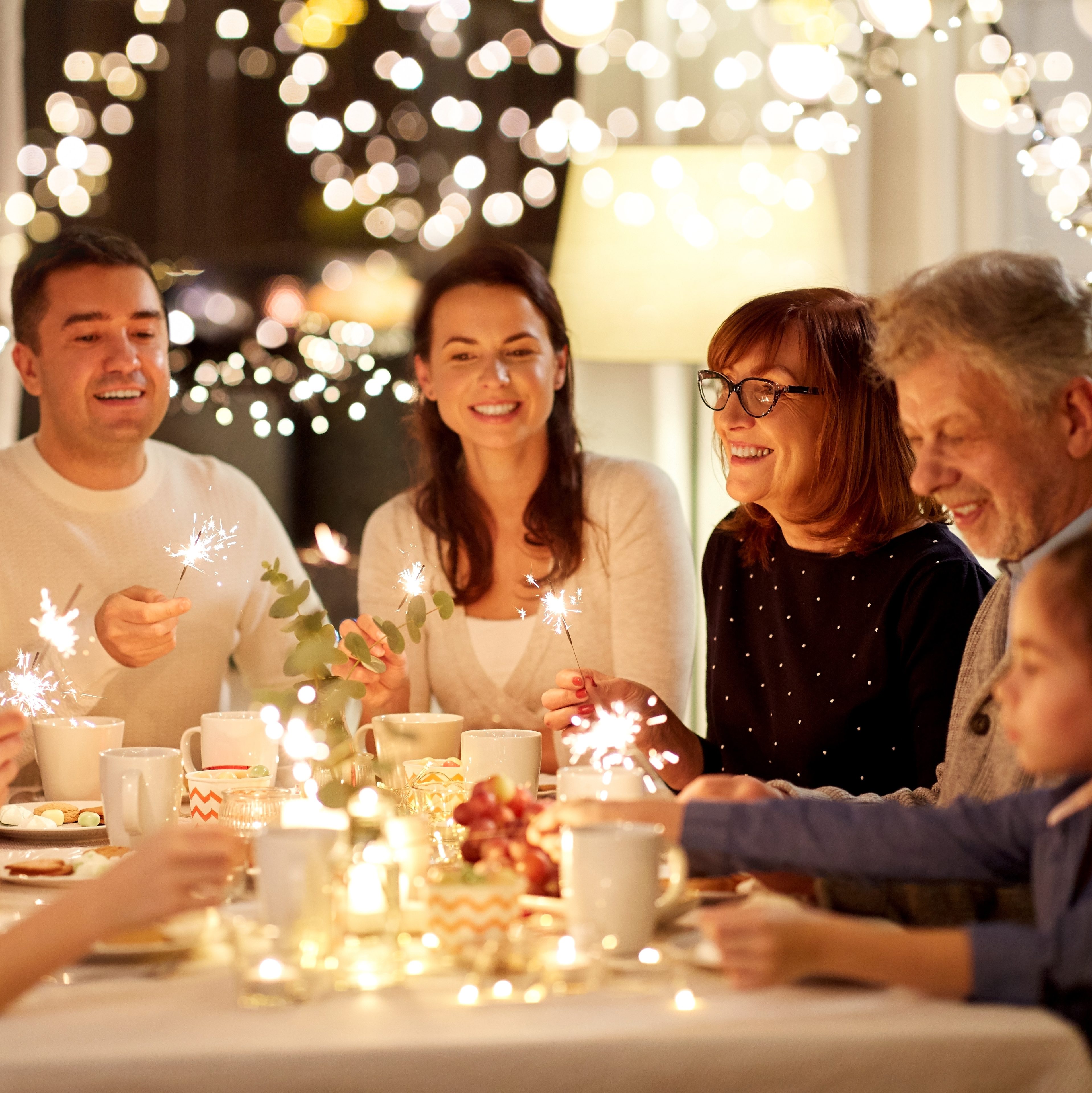 Family with sparklers sitting at the dining room table celebrating.