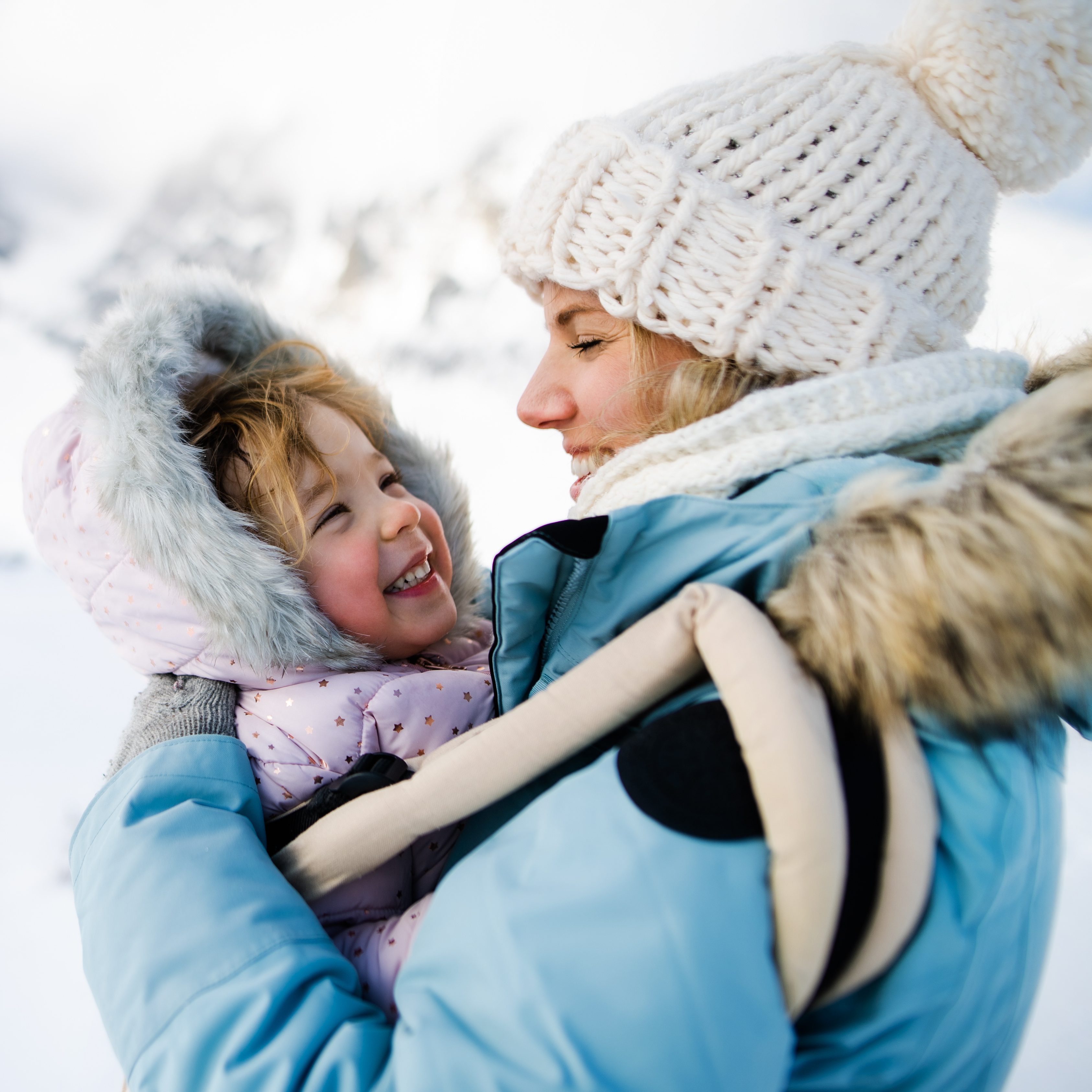 Mother with happy small daughter in carrier standing in winter nature.