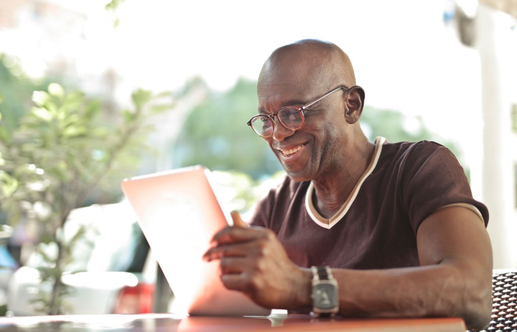 Mature man looks at at a tablet while sitting in an outdoor cafe.