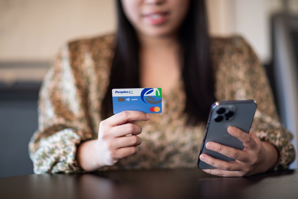 Customer holding a debit card in one hand and a phone in the other while making an online transaction.