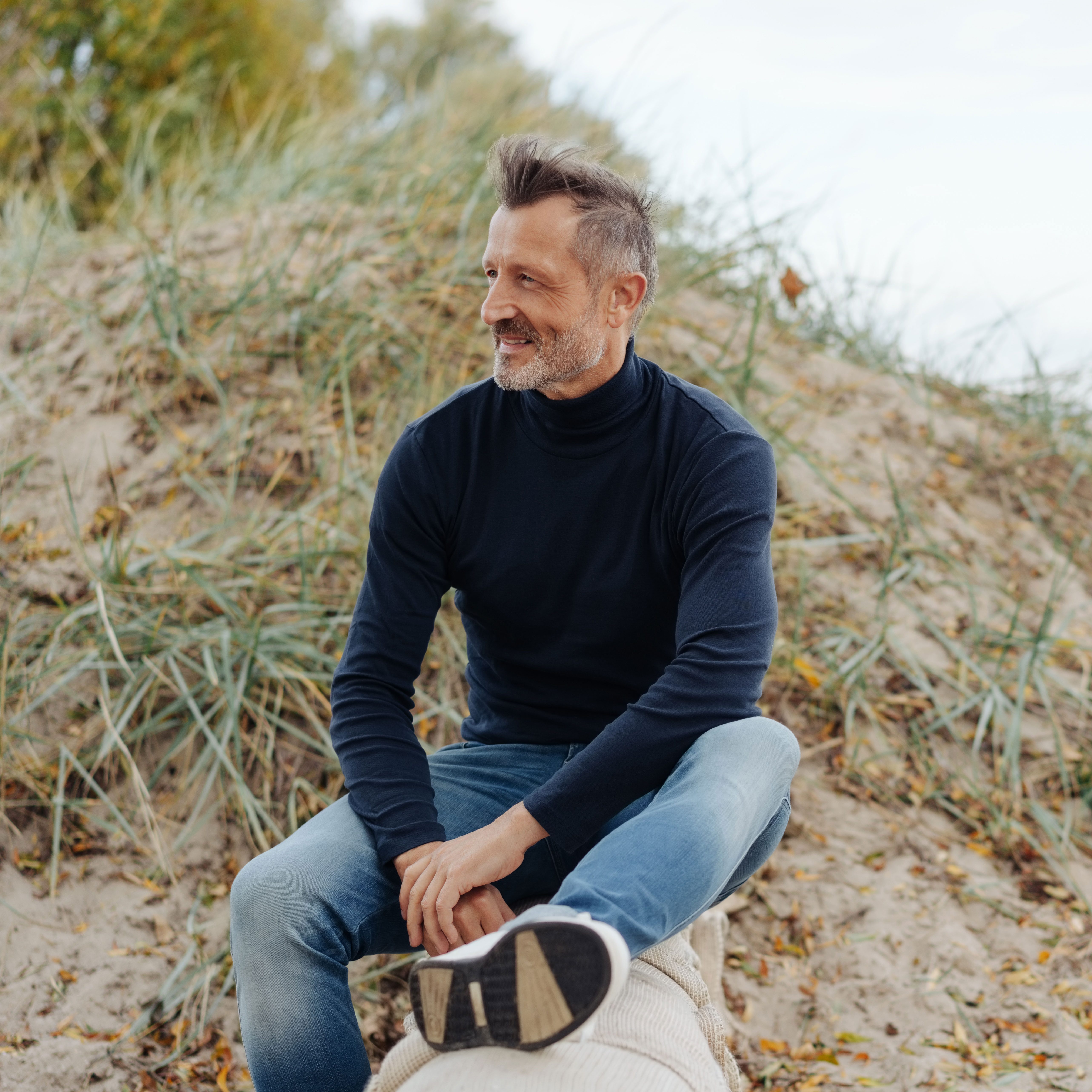 A man sits on a sand dune at the beach, relaxing.