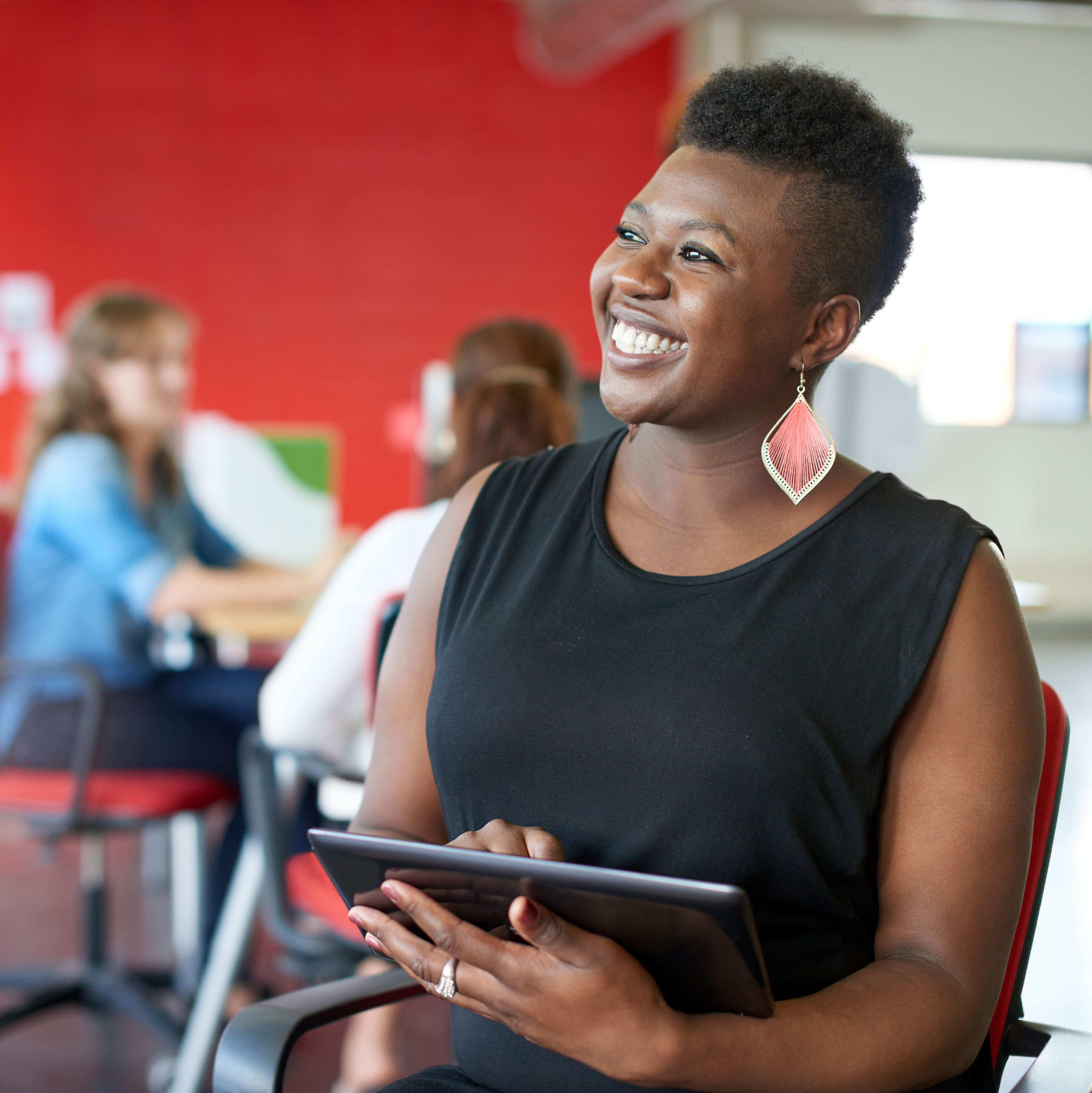 Business woman holds an iPad while sitting in an open office with co-workers.