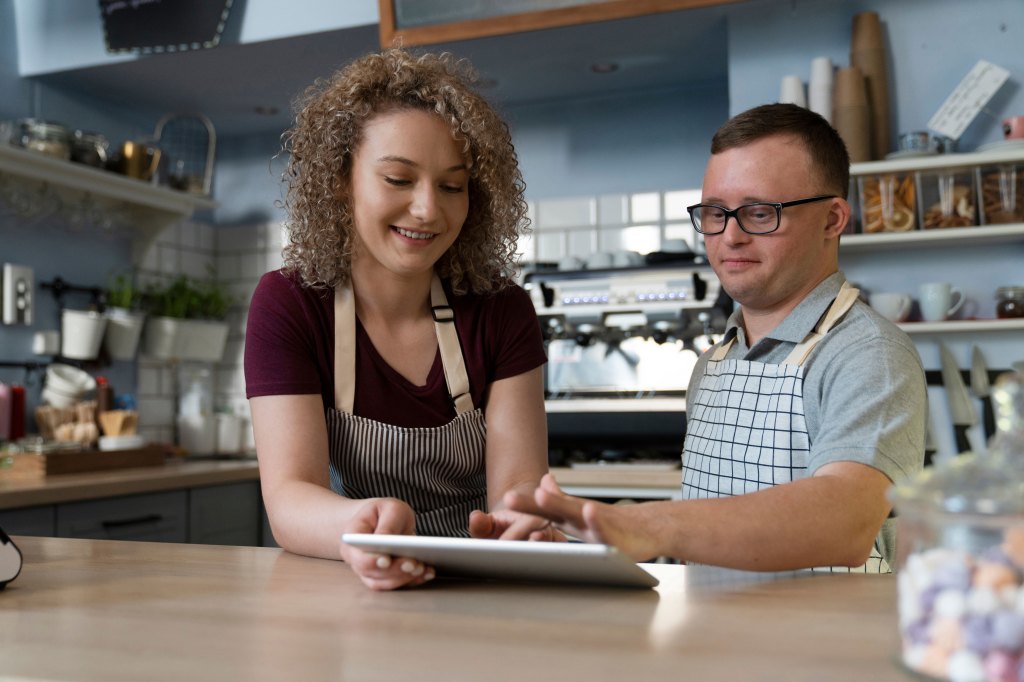 A cafe worker training an associate on a tablet how to take orders.