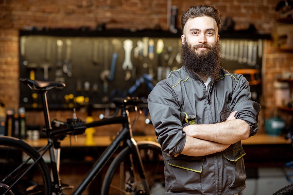 Bearded repairman in workwear at a bicycle workshop.