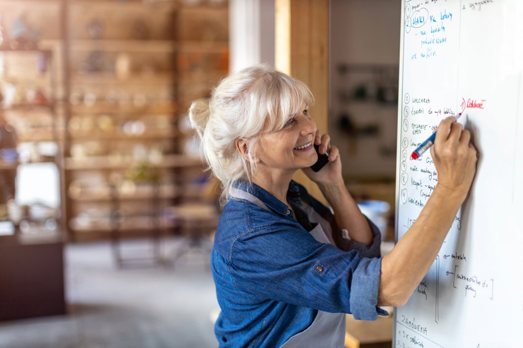 A senior female pottery artists takes a phone call in her studio.