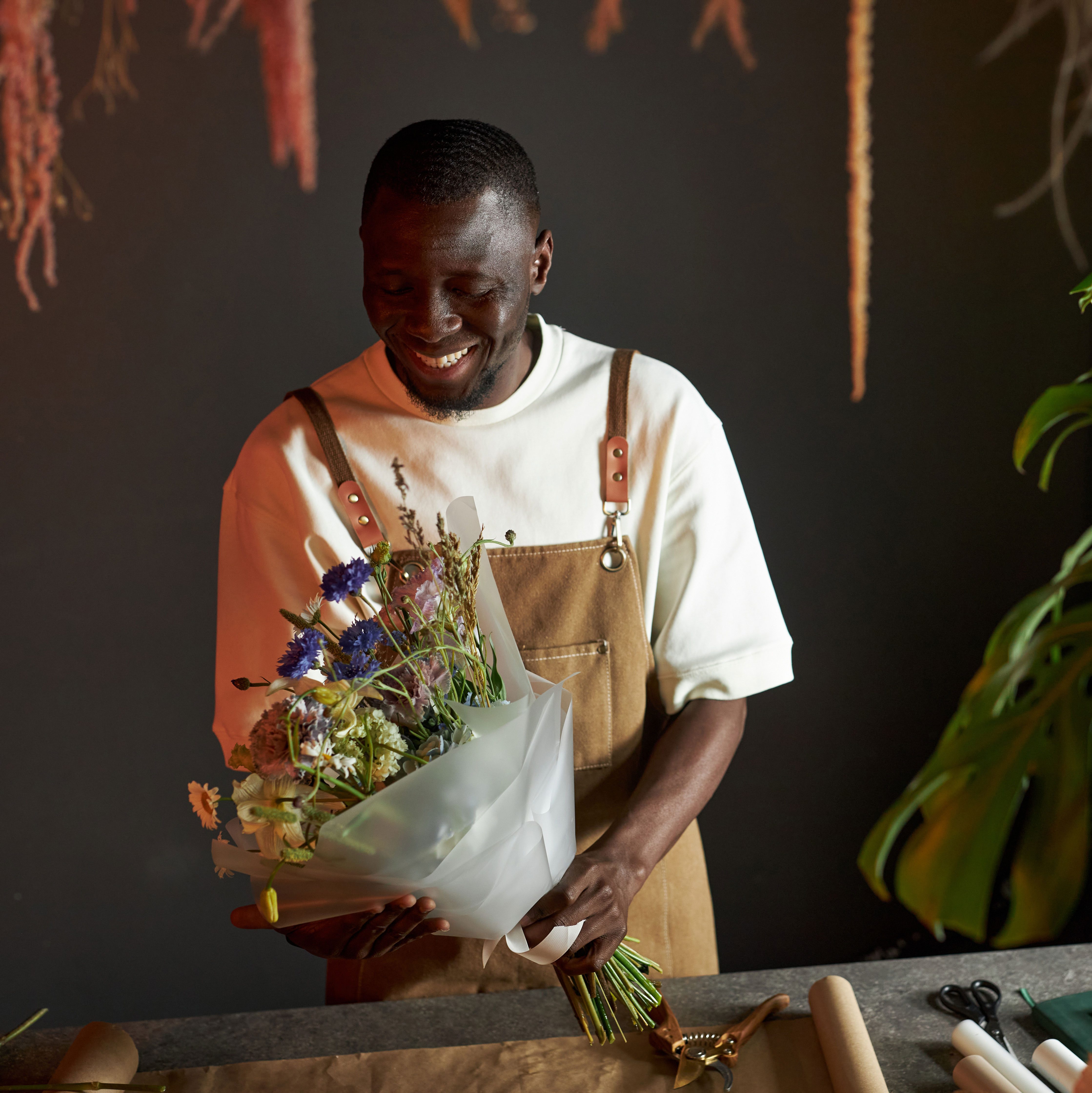 Waist up portrait of young man smiling while creating beautiful flower bouquet in elegant shop.